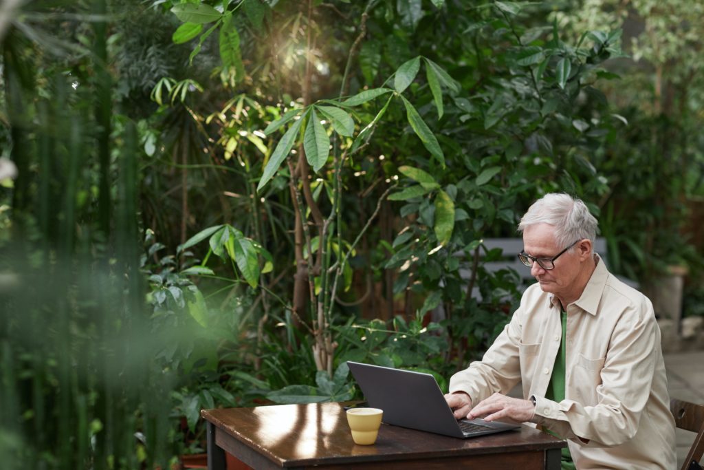 Man sitting in a garden at a table with a laptop working